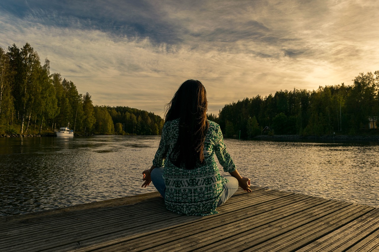 En kvinna sitter på en brygga vid en sjö i skymningen och göra yoga.