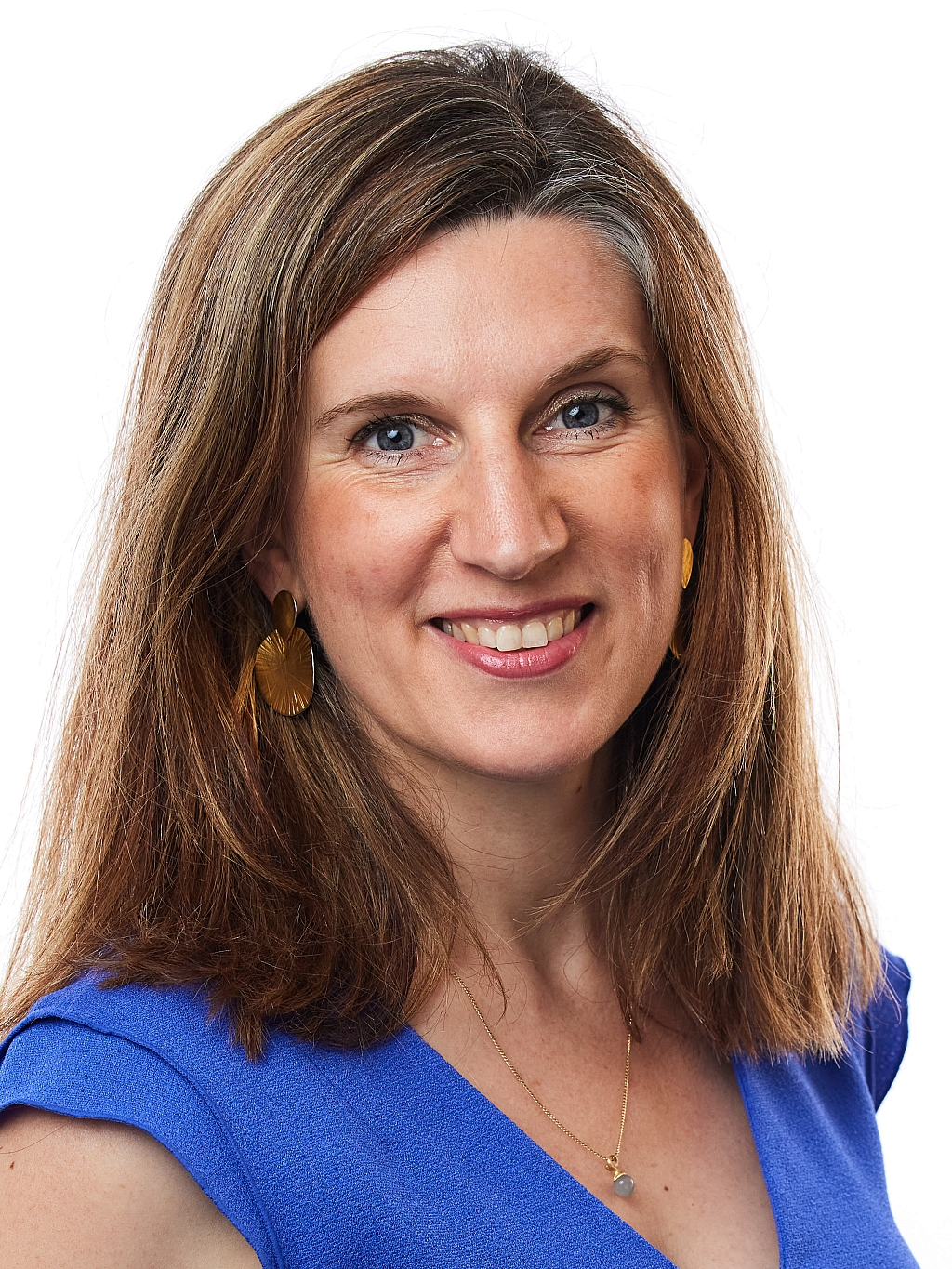 Woman wearing a blue top, gold earrings, and a necklace, smiling and facing forward against a white background.