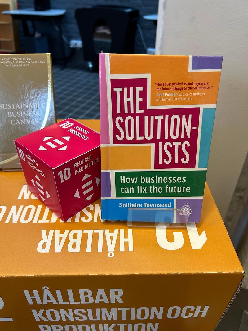 En bild på en bok som står på en box. Bredvid boken står en mindre box. Boken heter The Solutionists: How businesses can fix the future.