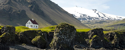 Ett vitt hus med isländska berg i bakgrunden. 