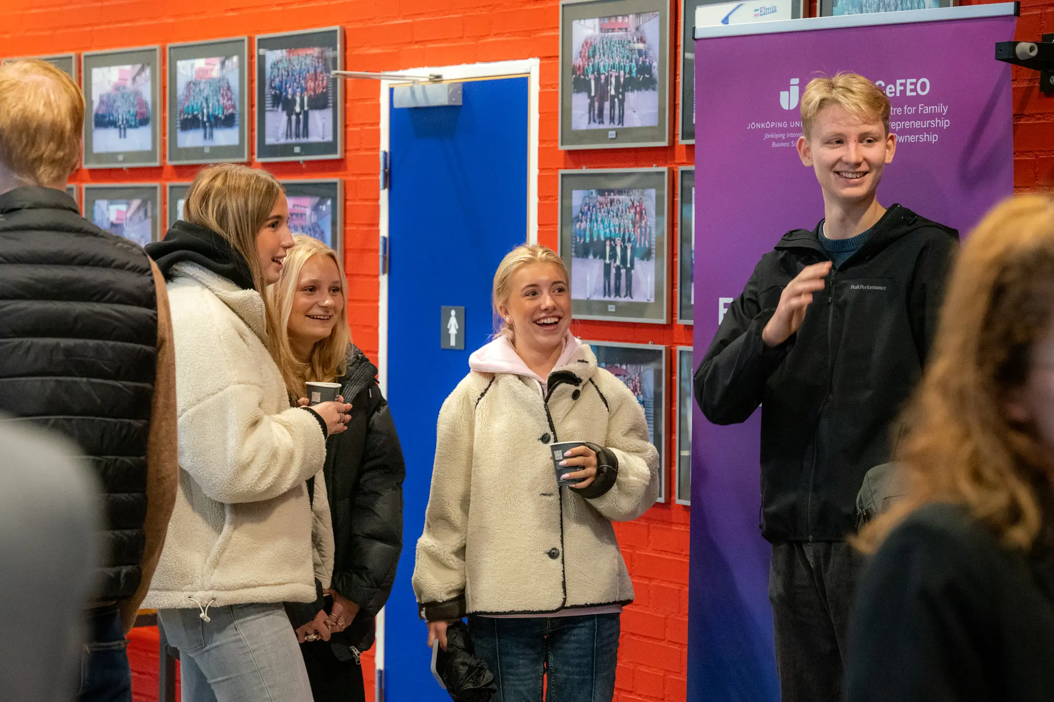 En grupp gymnasieungdomar ler och hälsar på någon.