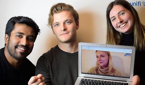 Three students looking happy, holding up a laptop with another student on the screen, also smiling. All four students are the winning team of the JIBS Entrepreneurship Challenge 2020. 