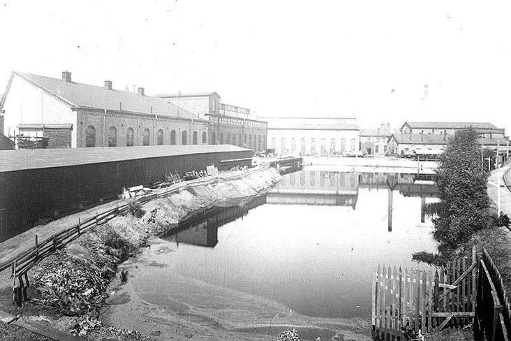 Factory buildings next to water in the JMW area. It is a historic photo in black and white.