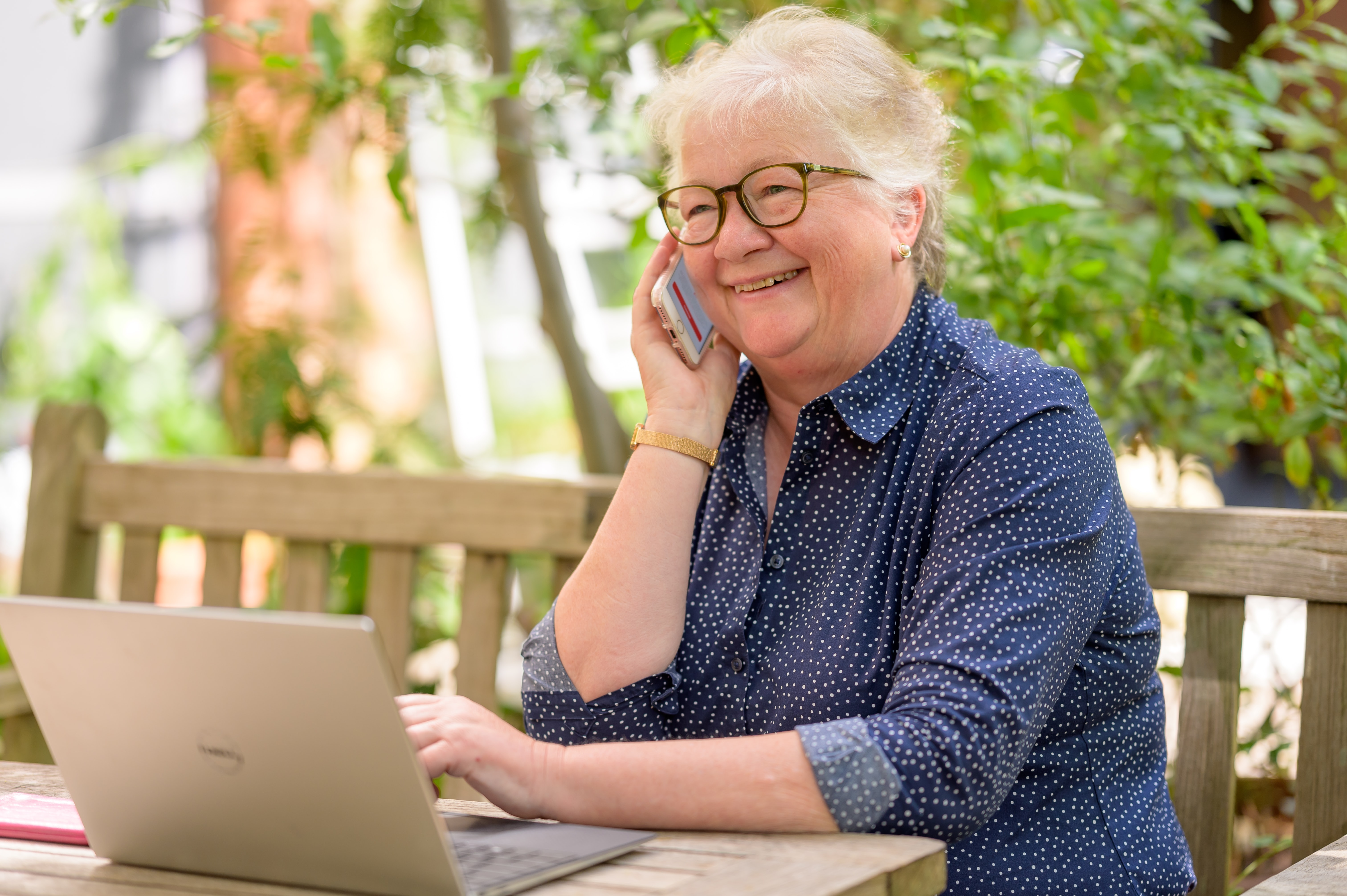 Äldre kvinna sitter utomhus med mobil och dator