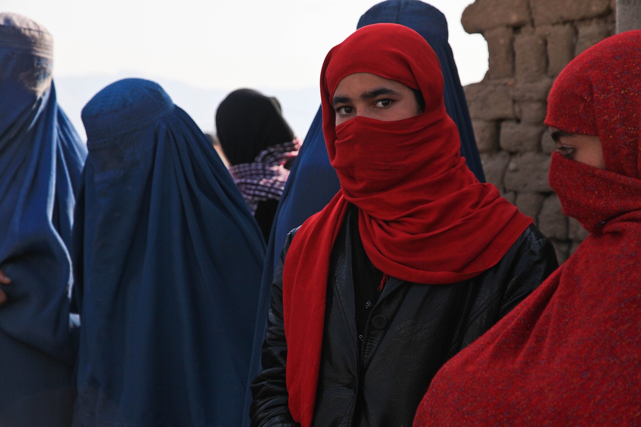 Kvinnor med täckta ansikten i blå och röda tyger, varav en tittar in i kameran. 